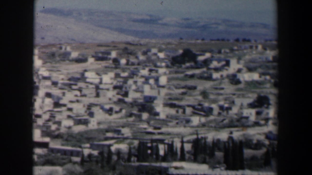 Town buildings and roads seen from above with hills beyond.