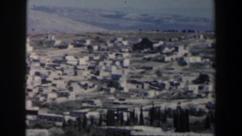 Elevated 1960 Israel town view showing clustered white buildings, winding roads, dark trees, and a broad dry hillside in the distance.