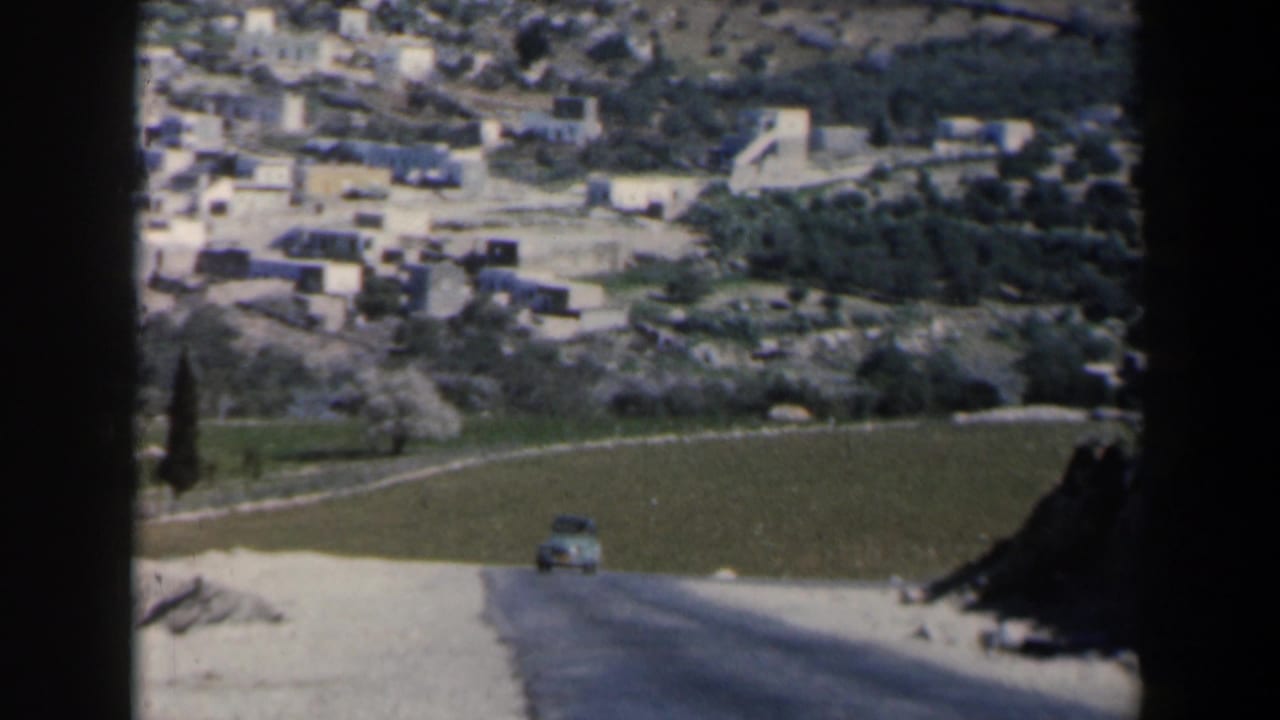 1960 Israel 8mm view of a road leading past fields toward clustered white hillside buildings, seen with soft home-movie focus.