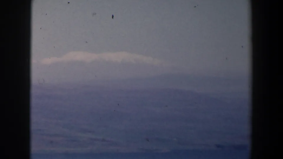 1960 Israel home-movie frame with a pale cloud band over distant mountain or hill forms, framed by dark 8mm edges.