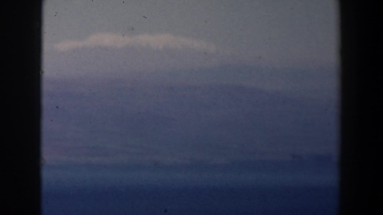 Blue ocean horizon beneath a pale cloudy sky with dark film borders.