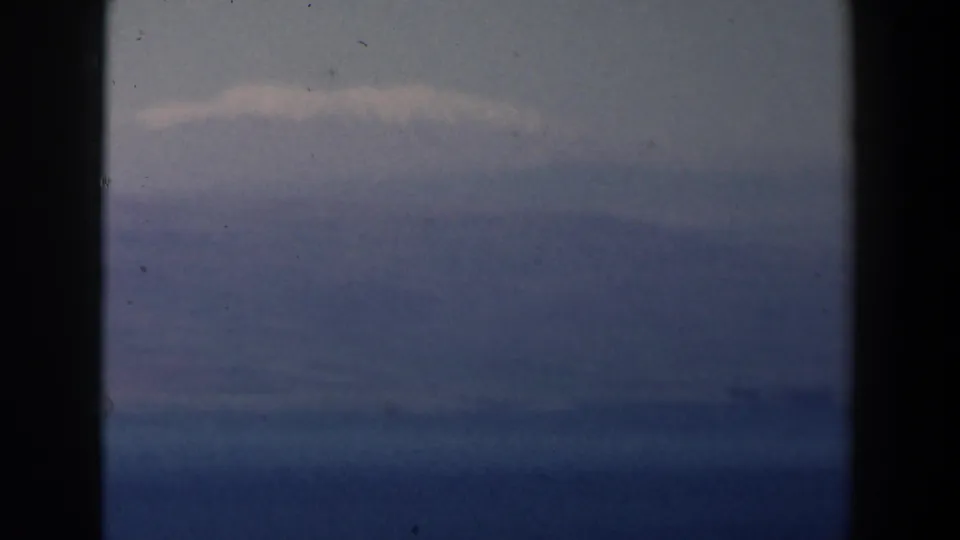 1960 Israel 8mm frame showing a blue sea horizon under thin clouds, with dust specks and dark gate edges.