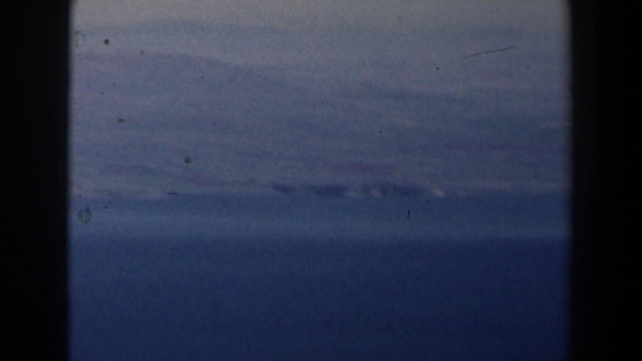 Distant sea horizon and pale clouds framed by dark vertical film edges.