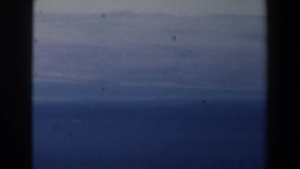 1960 Israel 8mm still of open water beneath a pale cloud band, with grain, dust, and dark borders visible.