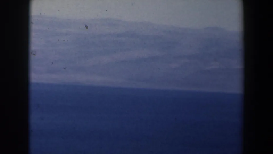 1960 Israel coastal frame showing layered clouds above a blue sea, with home-movie grain and gate-edge shadows.