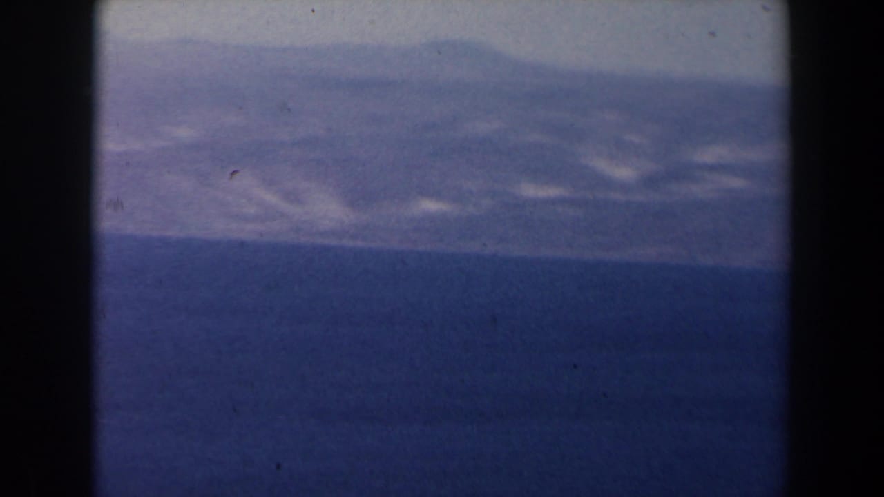 1960 Israel 8mm frame showing a blue lake and hazy mountain ridge, with dark gate borders and soft faded color.