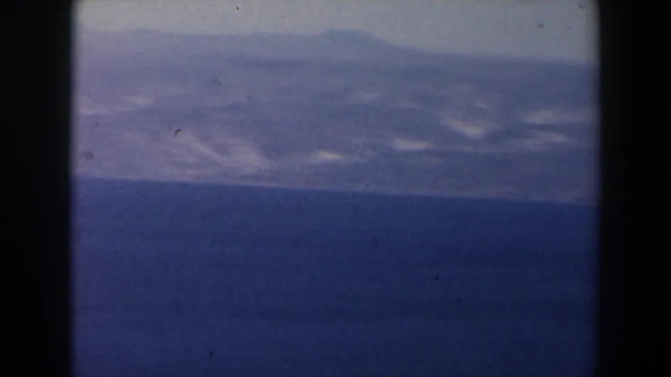 1960 Israel 8mm frame showing a blue lake and hazy mountain ridge, with dark gate borders and soft faded color.
