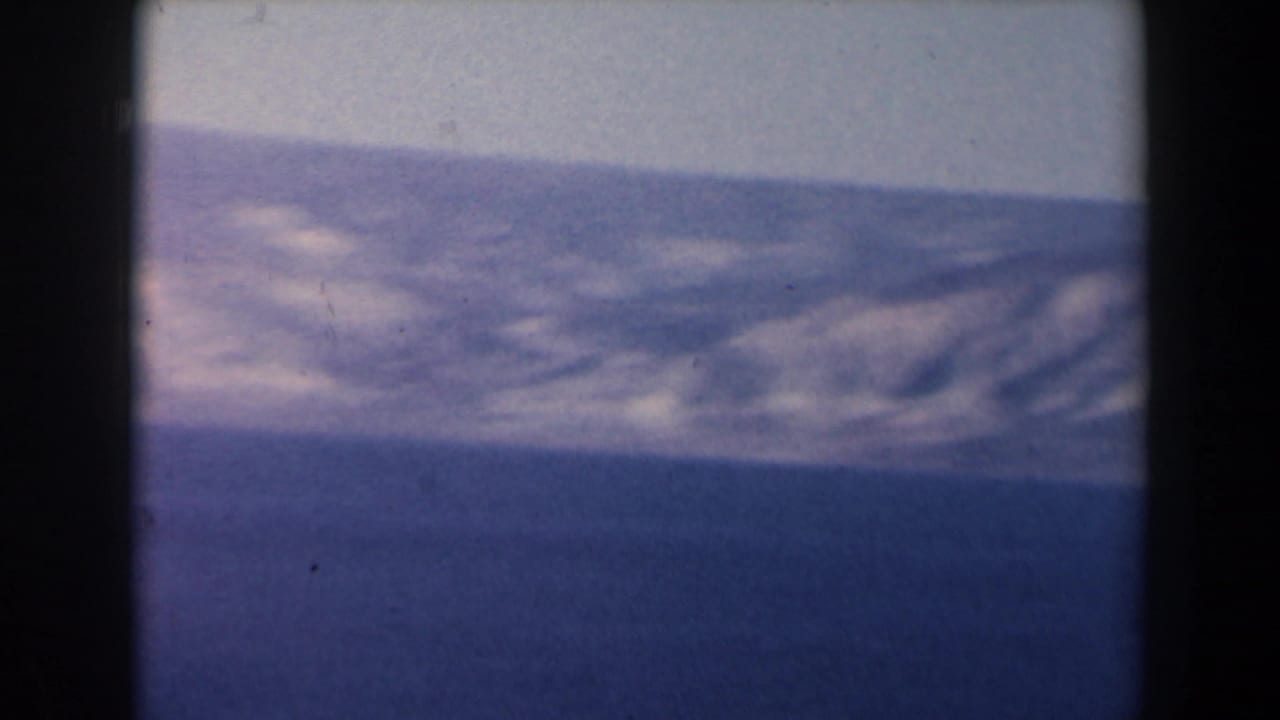 1960 Israel 8mm frame with blue water in the foreground and a pale mountain range beyond, softened by haze and film grain.