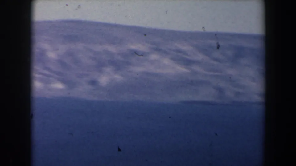 1960 Israel 8mm frame showing a hazy mountain slope beyond a blue lake, with visible dust, grain, and gate shadowing.