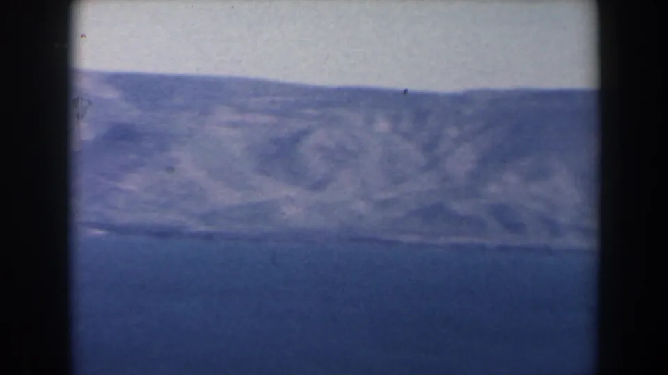 1960 Israel 8mm frame with the lake below a pale mountain ridge, showing faded color, soft focus, and visible film wear.