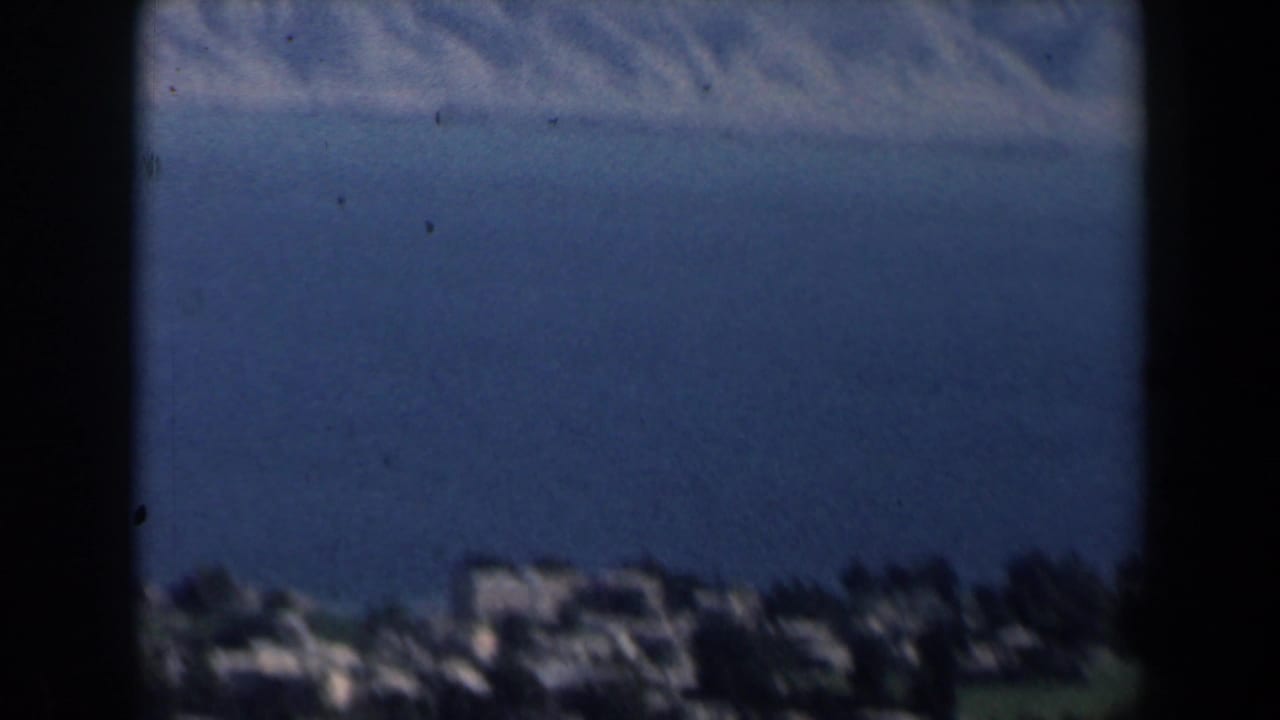Blurred coastal buildings below a blue sea horizon, framed by dark vertical edges.