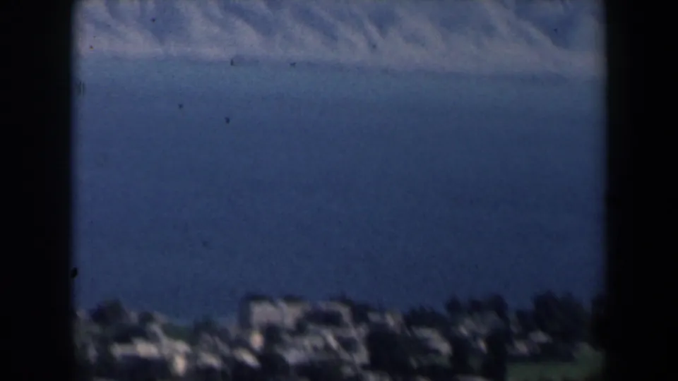 1960 Israel 8mm frame with distant coastal buildings, blue sea beyond them, and soft handheld focus.