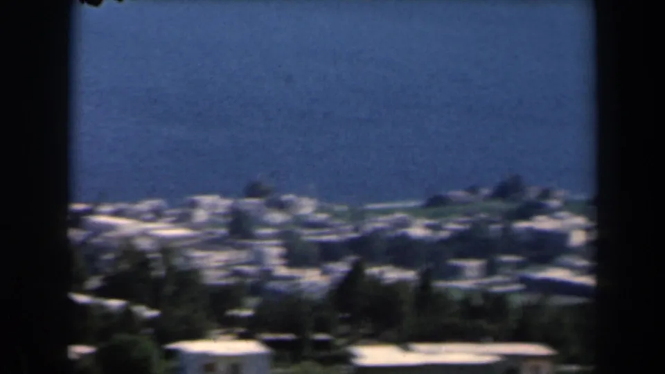 Elevated 1960 Israel home-movie view of a hillside coastal town with white and tan buildings near blue water.