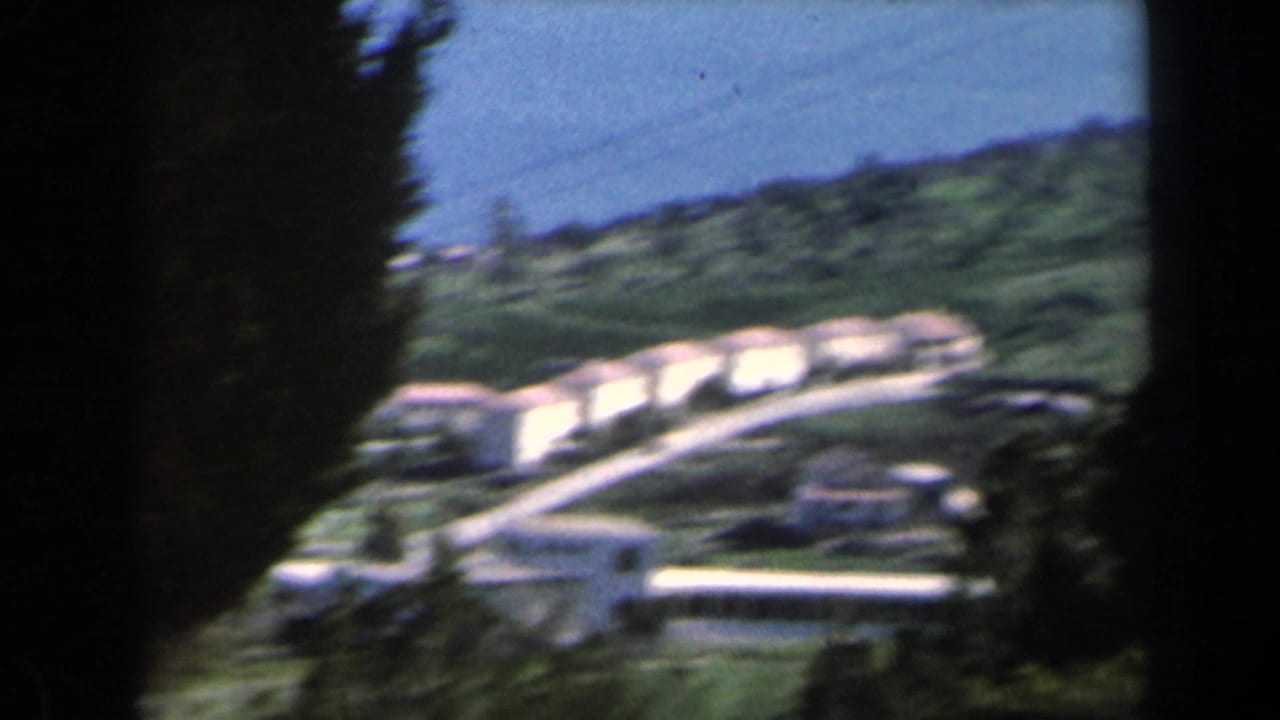 White hillside buildings and roads seen through dark vertical framing near a blue coastal horizon.