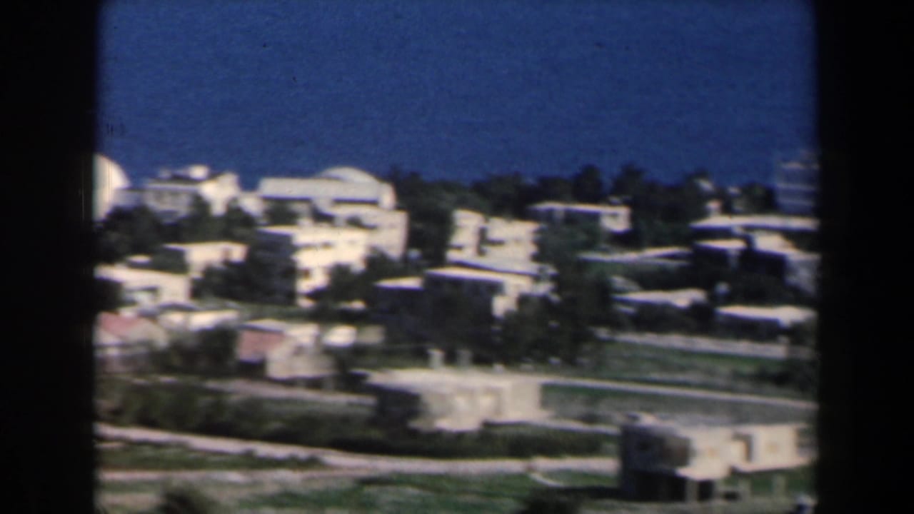White low-rise buildings on a green hillside beneath a deep blue sky.