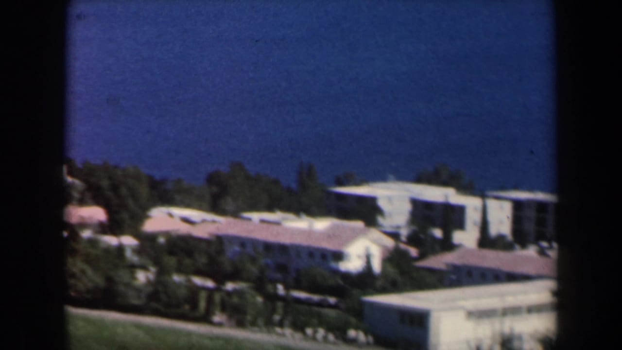 1960 Israel 8mm frame with distant low-rise housing, red-tiled roofs, trees, and open green slopes.