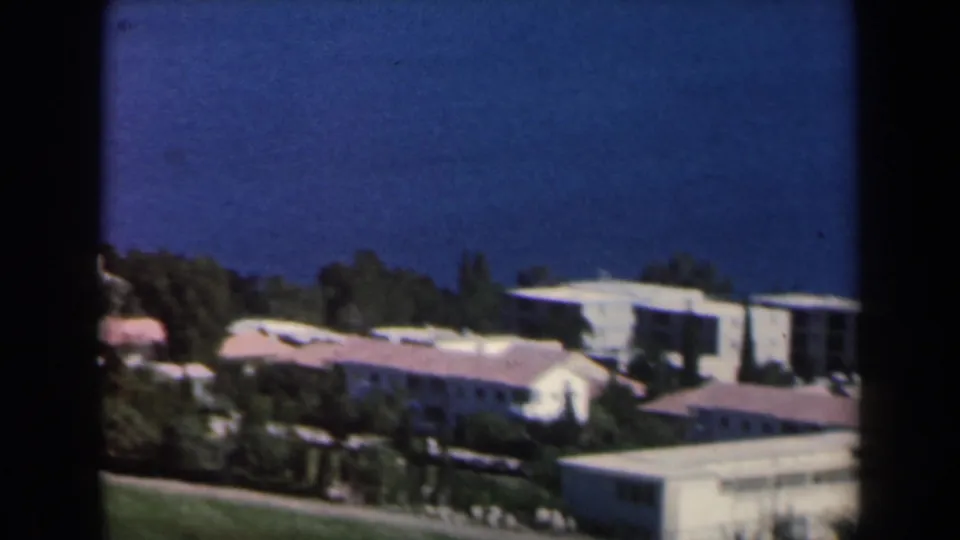 1960 Israel 8mm frame with distant low-rise housing, red-tiled roofs, trees, and open green slopes.