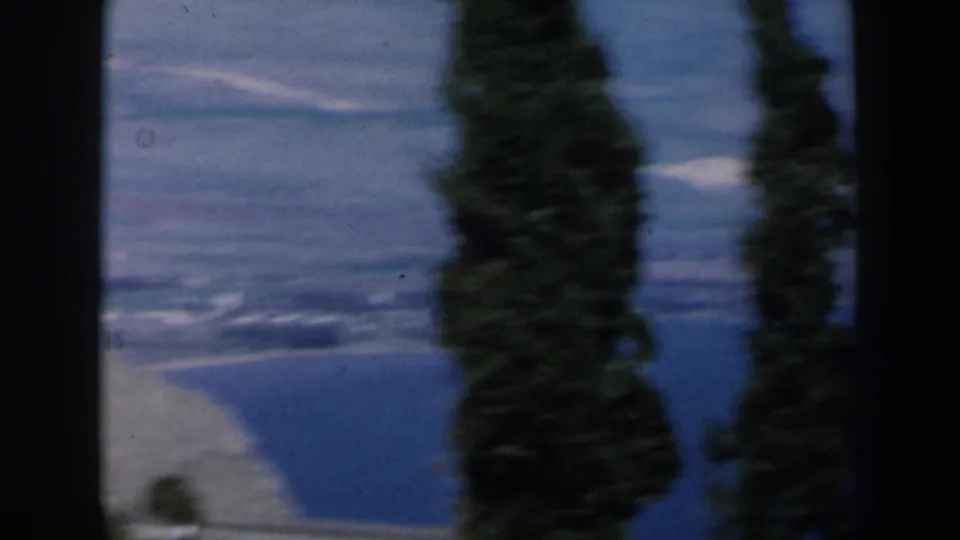 1960 Israel 8mm frame with a blue coastal water view, shoreline, trees, and heavy gate-edge shadowing.