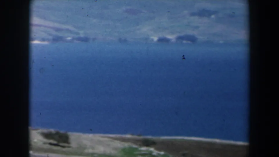 Soft 8mm view from Israel in 1960, looking past coastal land and fields toward blue water and a pale shoreline under hazy light.