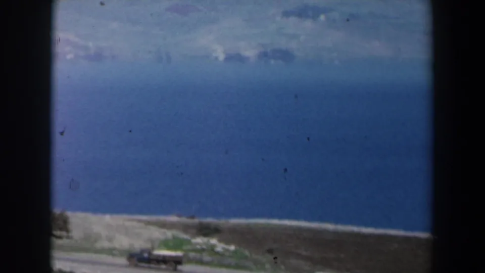 1960 Israel 8mm frame showing a lake, pale shoreline, road, and distant hills under a bright sky.