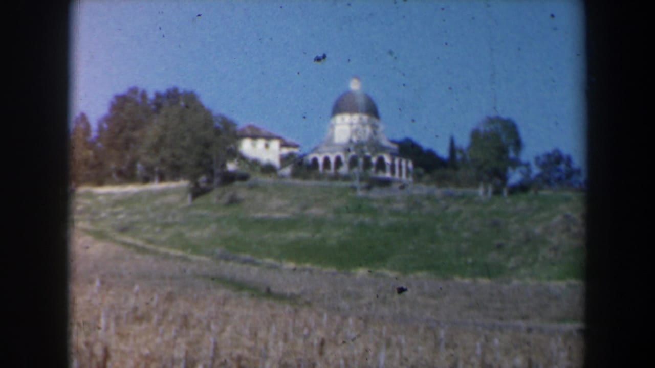 Distant domed building on a green hillside above a dry field.