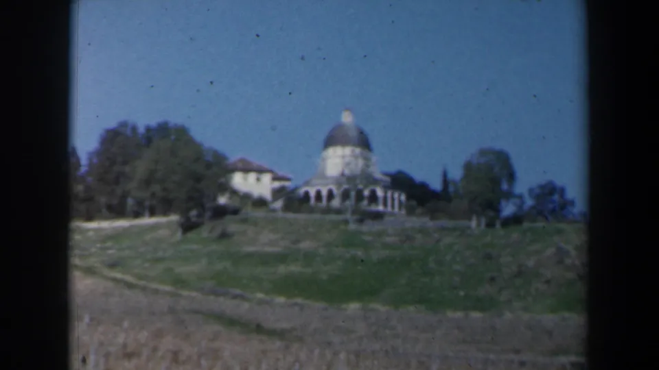 1960 Israel 8mm frame showing a distant domed hilltop building beside trees under a clear sky.