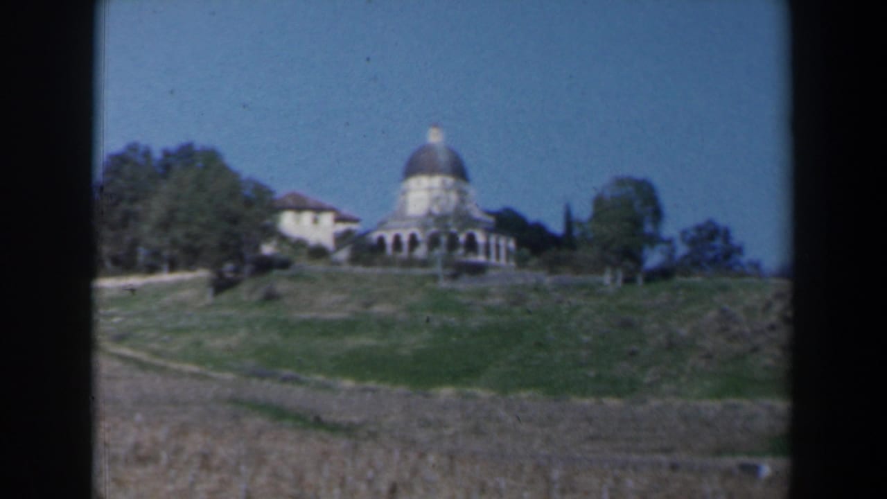 Hilltop domed building seen from below with trees and open ground.
