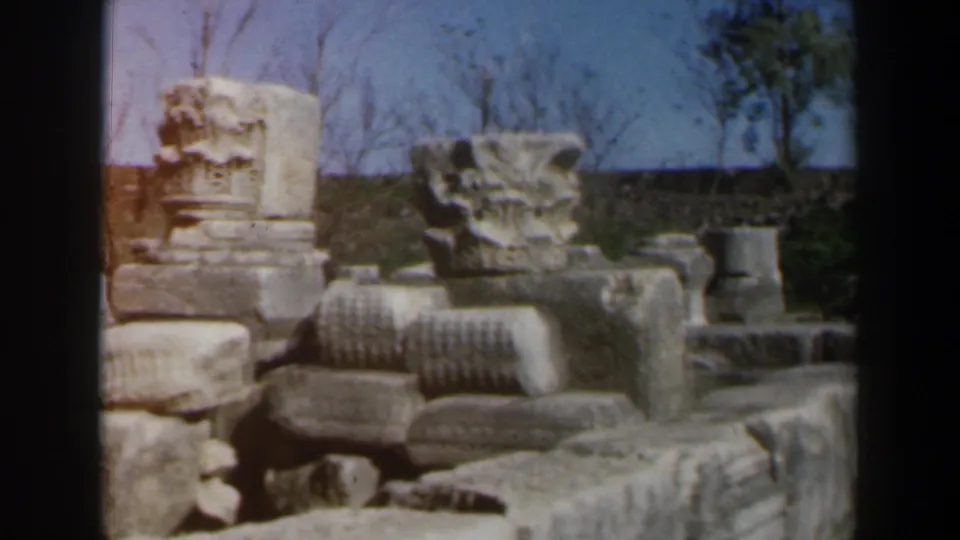 1960 Israel 8mm frame showing outdoor stone ruins, carved blocks, and column-like fragments.