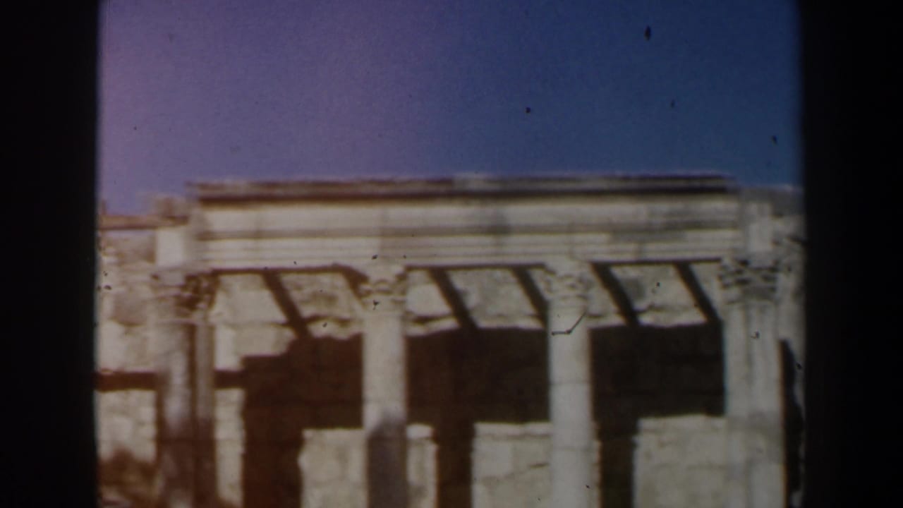 Sunlit stone ruin facade with columns, dark openings, and a blue sky above.