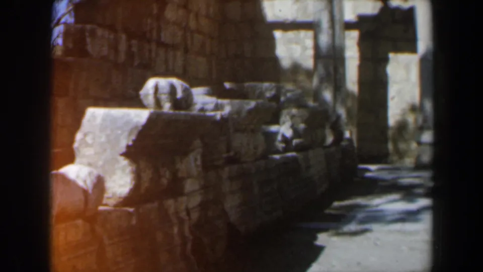 1960 8mm travel footage from Israel showing a low stone wall and columned ancient masonry in harsh sunlight.