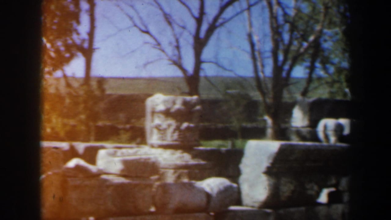Stone ruins and carved fragments seen through dark film-frame edges under a blue sky.