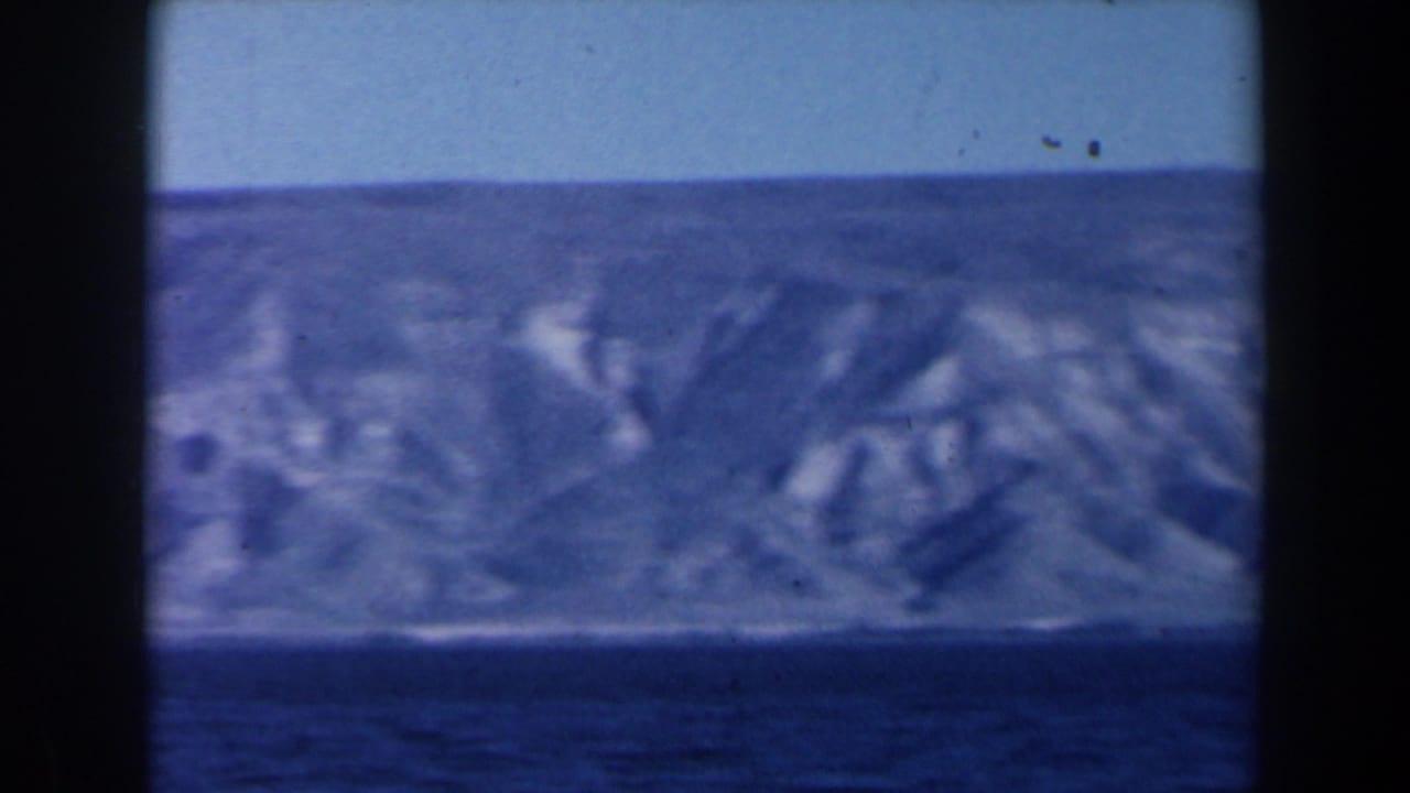 1960 8mm Israel footage looking from the water toward a rugged, pale coastline under a clear blue sky.