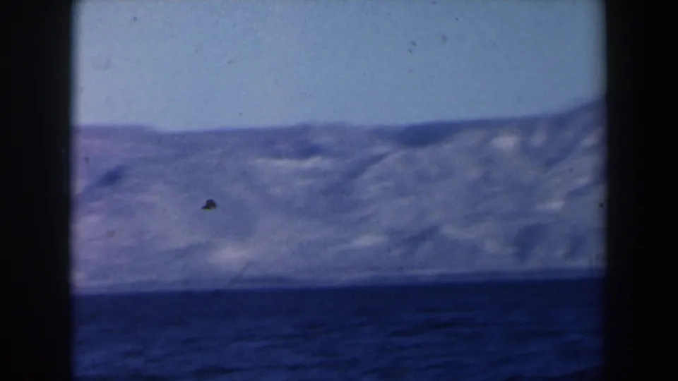 1960 8mm Israel footage with open sea in front of a rugged distant shoreline, framed by dark home-movie borders.