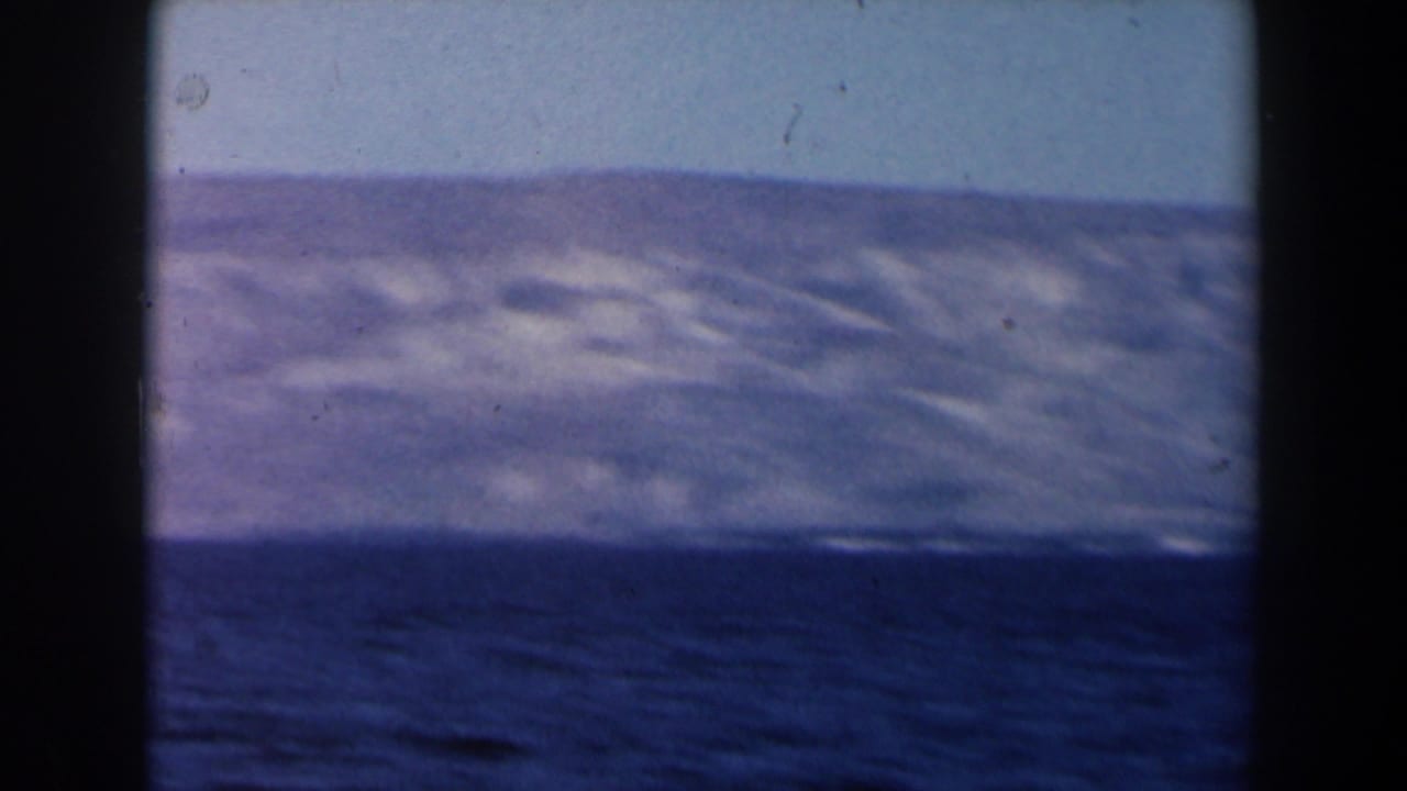 1960 Israel-labeled 8mm frame showing a dark blue sea and distant hazy mountains beneath a pale sky.
