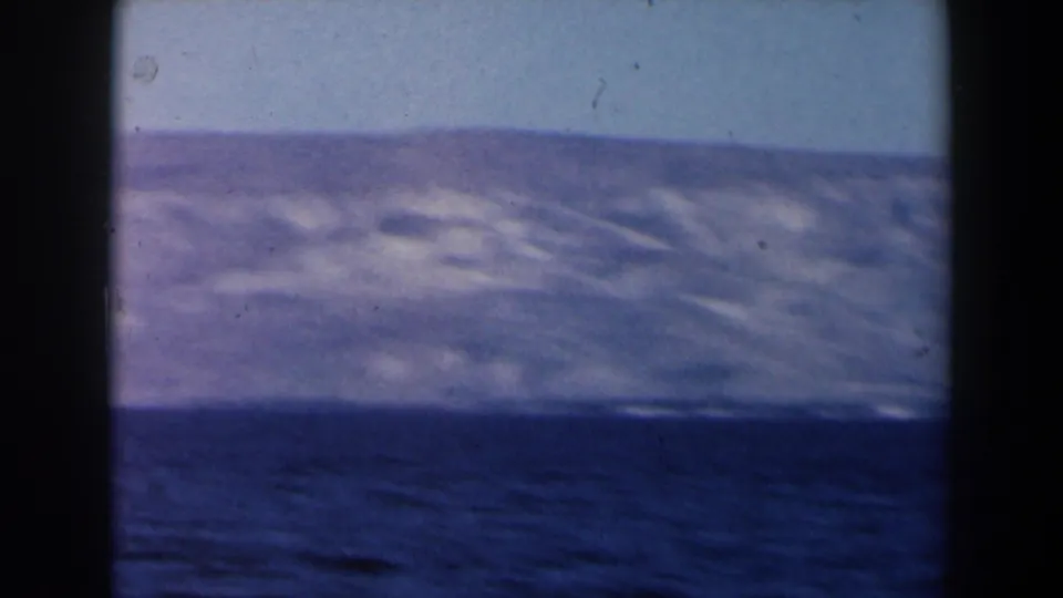 1960 Israel-labeled 8mm frame showing a dark blue sea and distant hazy mountains beneath a pale sky.