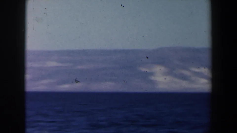 1960 Israel-labeled 8mm frame showing a low mountain ridge across calm water with faded blue-lavender tones.