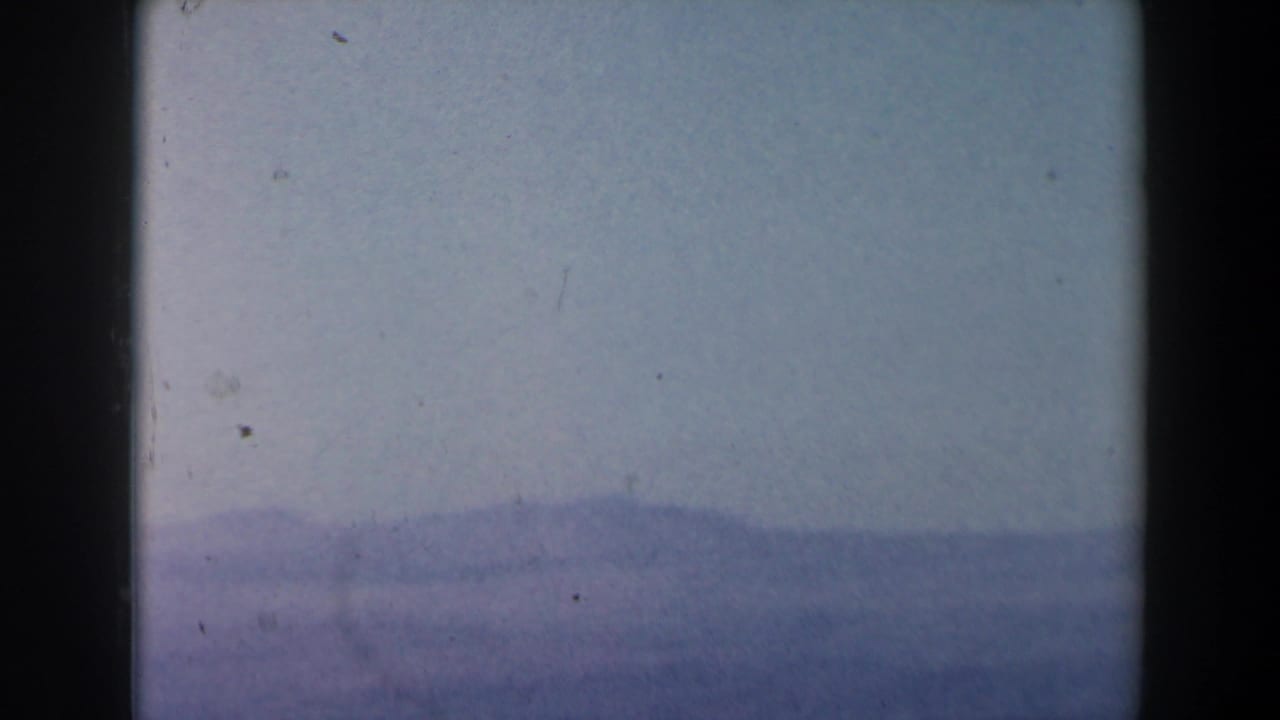 Hazy seascape with distant landforms under a pale sky, bordered by dark film edges.