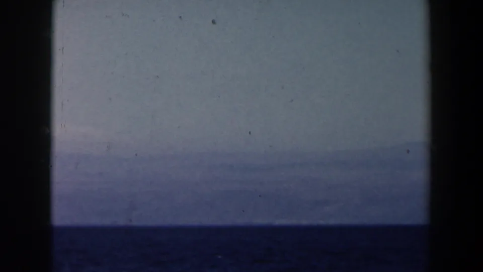A distant hazy shoreline or mountain range appears above dark blue water in 1960 Israel-context 8mm footage.