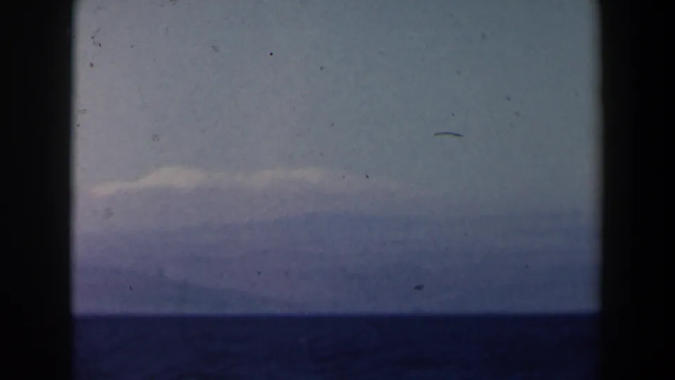 Handheld 1960 8mm Israel-context seascape with pale haze, distant cloud or land band, and dark ocean below.
