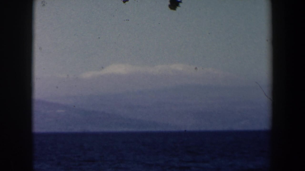 1960 8mm Israel home-movie frame showing open water and a distant hazy mountain range through dark film-frame borders.