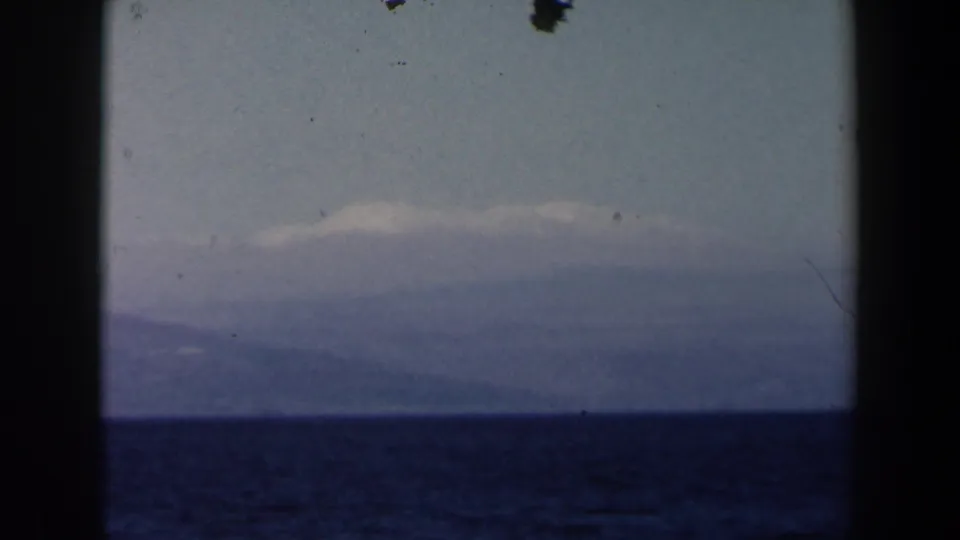 1960 8mm Israel home-movie frame showing open water and a distant hazy mountain range through dark film-frame borders.
