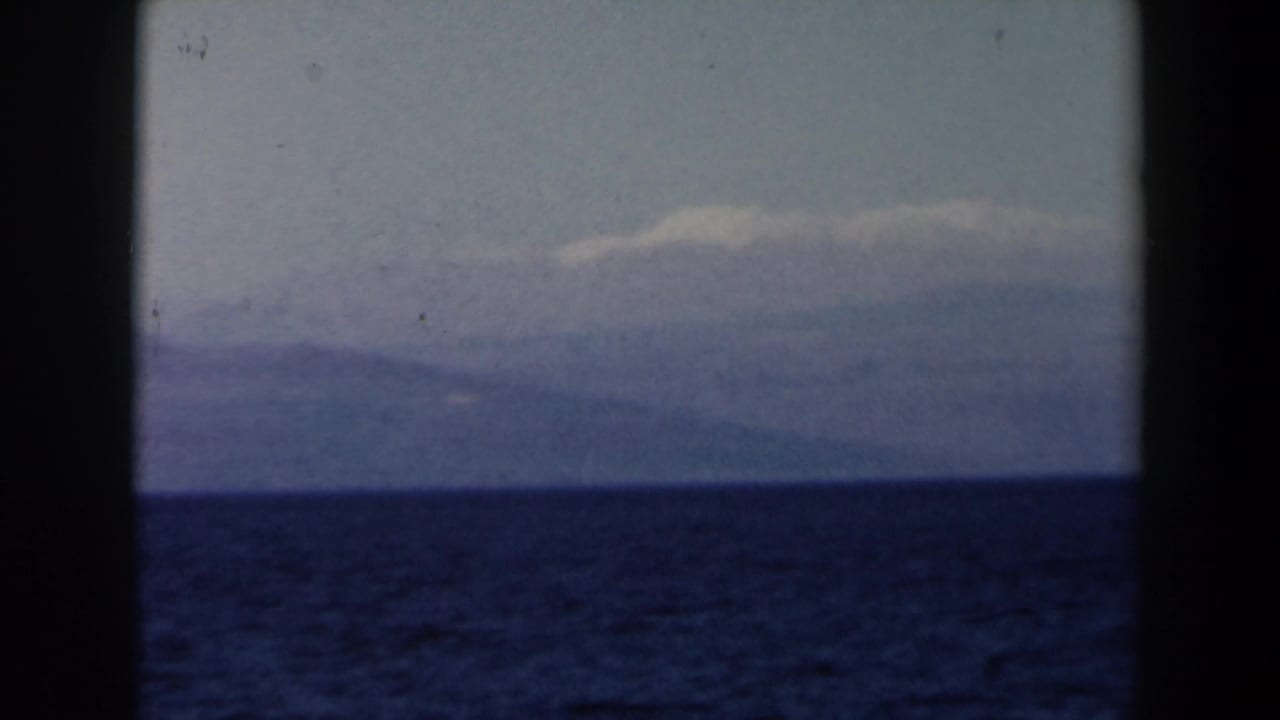 Dark blue sea and pale sky with a distant mountain mass across the horizon.
