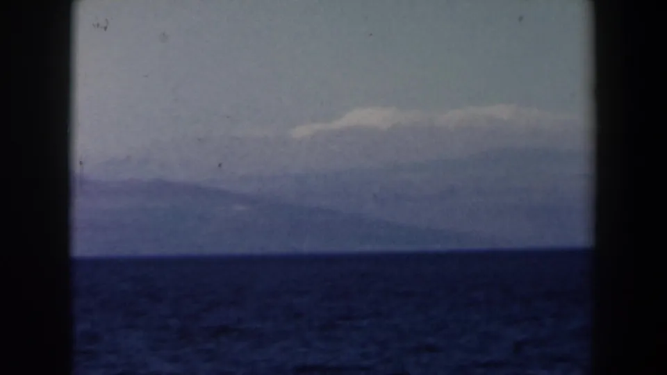 1960 8mm Israel seascape frame with dark blue open water, pale sky, and a distant mountainous landform on the horizon.