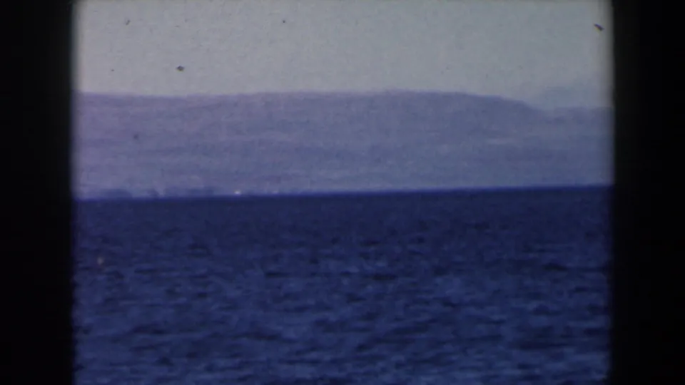 1960 Israel 8mm home-movie view across open sea toward a low, hazy mountain range in soft blue-purple color.