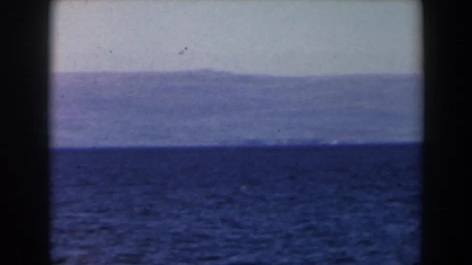 1960 8mm Israel travel frame showing open water, a distant hazy shoreline or mountain range, and visible dark gate edges.