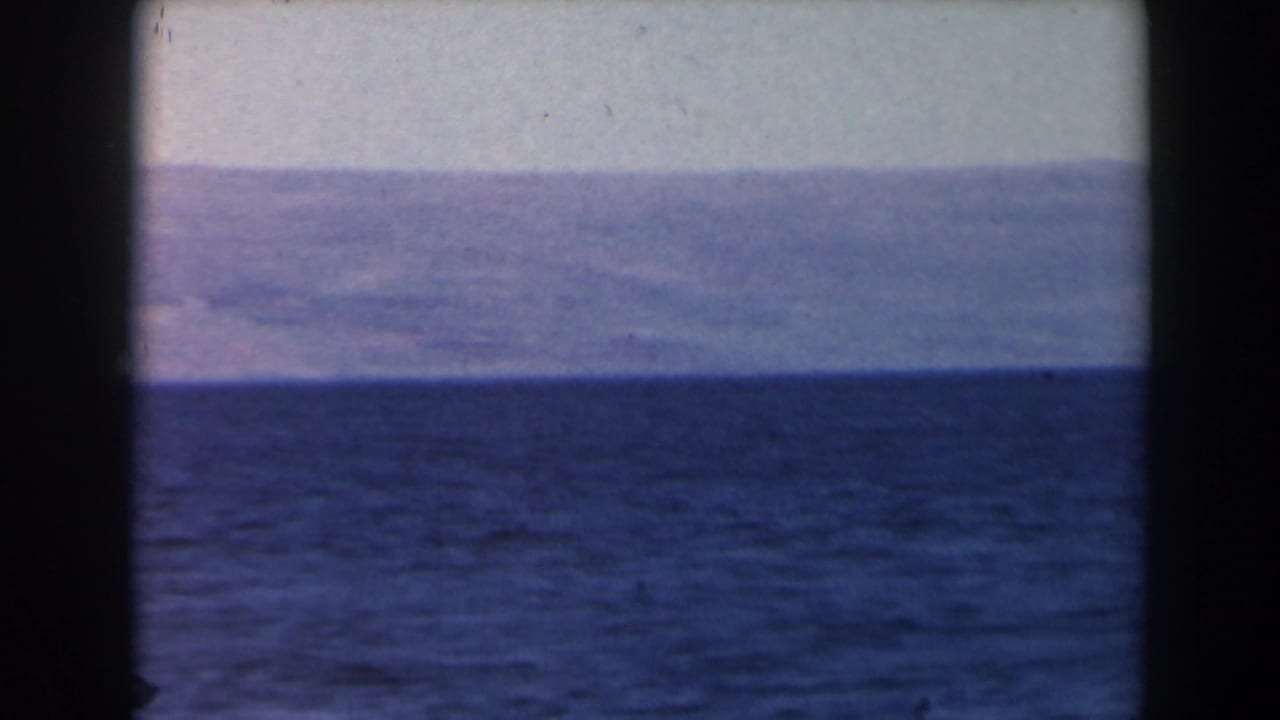 Dark blue sea beneath a pale sky with hazy mountains on the horizon.