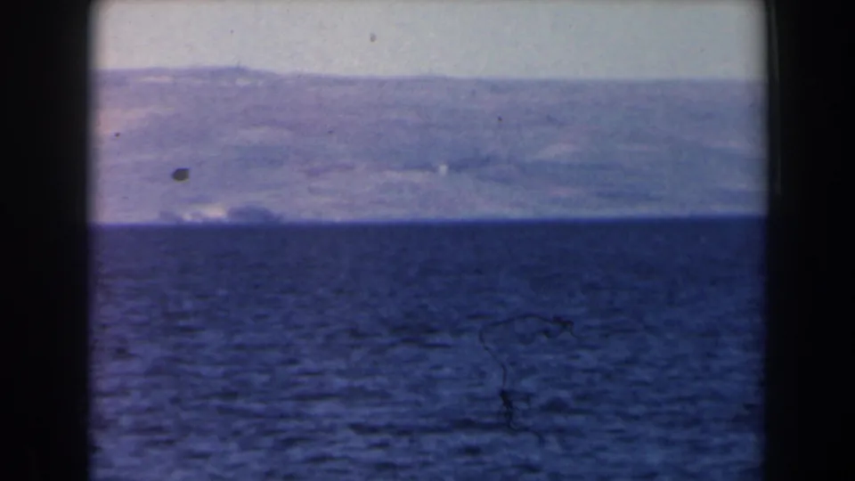 1960 Israel 8mm frame with rippled sea in the foreground and a hazy mountainous coastline beyond the horizon.