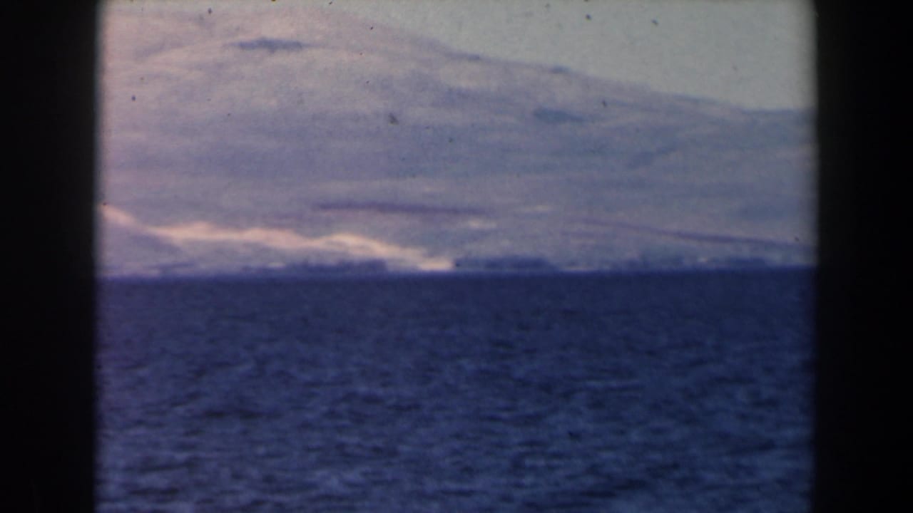 Blue ocean beneath a hazy shoreline and pale hills, bordered by dark film edges.