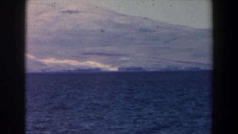 1960 Israel 8mm frame showing blue water, a distant hazy shoreline, pale hills, and dark vertical film-frame borders.