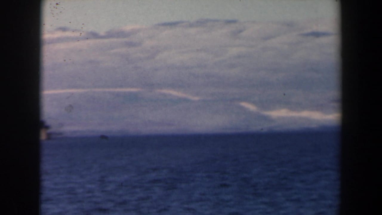 Distant hills and blue water seen across a dark vertical film-frame divider.